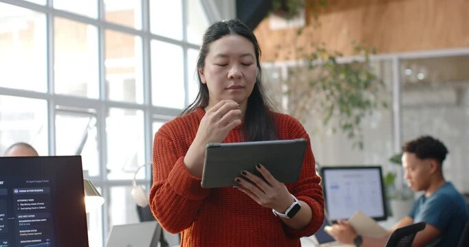 Diverse team Asian woman placing tablet using pen pausing, reviewing, resuming tapping in office