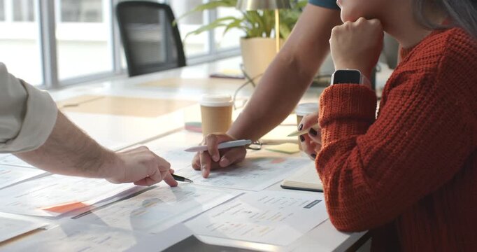 Colleagues pointing, tracing charts while woman in red knit reaching for pink highlighter