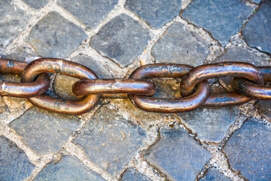 Rusty metal chain laying on old cobblestone pavement