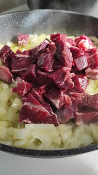    Trozos crudos de carne de ternera cortada en dados, colocada sobre una base de cebolla picada en una sart&eacute;n con aceite, para preparar estofado. Carrillada de ternera. 