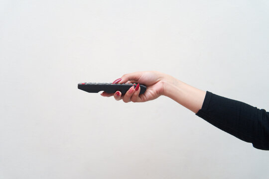 Close up of female hand holding TV remote control isolated on white background for International Television Day concept, media consumption, entertainment, and broadcasting