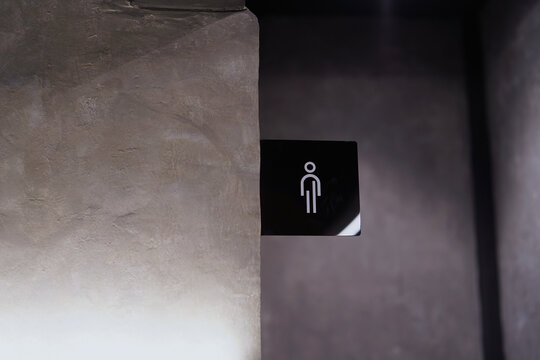 Modern Black Men's Restroom Sign on Textured Concrete Wall in Dimly Lit Interior. representing modern industrial interior design and public facility wayfinding.