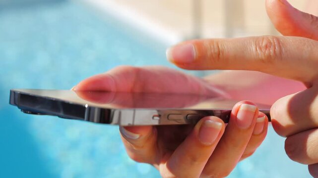 Close-up of female hands typing on a smartphone by a pool