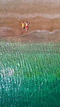 Couple in swimsuits lay on a sandy beach, top down view. Vertical