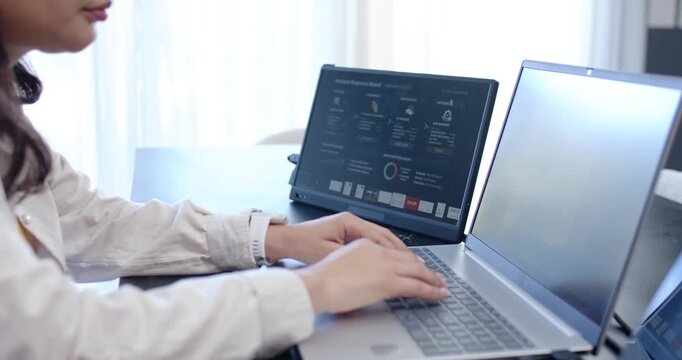 Woman starting by typing on laptop at desk, reviewing dashboard on second screen, pausing to think