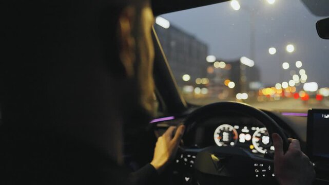 Backseat view on man driving car through the streets of the evening city.