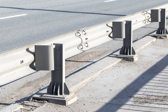 Closeup view of a metal guardrail and support posts along an urban highway, highlighting safety barrier construction, pavement edge, bolts and shadows for transportation infrastructure