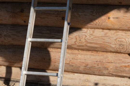 Aluminum ladder leaning against a sunlit log cabin wall, highlighting natural wood grain