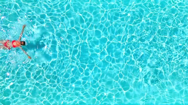 Top down view of a woman in pink swimsuit swimming on her back in the pool.