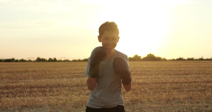 Child practices boxing in rural field at sunset, throwing punches with gloves. Active outdoor training represents confidence, strength, healthy childhood and perseverance through sport and growth.