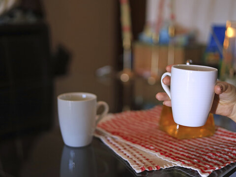Hand holding a white mug, ceramic drinkware and tableware in home beverage service and everyday refreshment