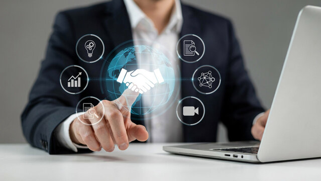 Businessman's hand touching glowing handshake icon with global network and business symbols during digital collaboration