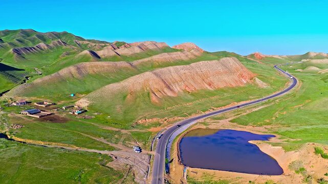 Aerial view of a winding road and a calm pond beside rolling hills and barren mountain ridges along the S101 highway in Xinjiang, China.