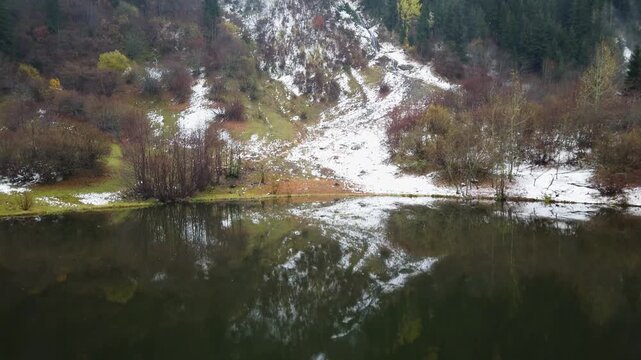 Mountain lake in the Artvin highlands, Turkey, with the first snow dusting the autumn slopes, bare shrubs and conifer forest mirrored in the dark still water