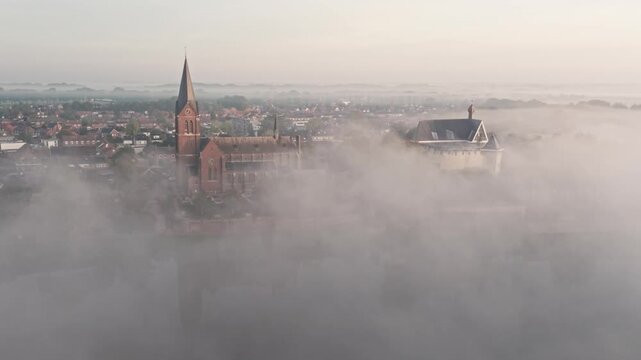 Aerial view of Kasteel de Keverberg and the historic church emerging from thick morning fog in Kessel, Limburg, Netherlands.