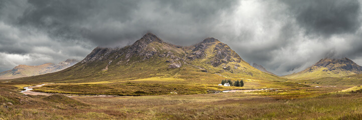 Panoramic view of the River Coupall passing by the Wee White House at Glencoe in the Highlands of Scotland with Buachaille Etive Mor and Buachaille Etive Beag shrouded in dark rain clouds behind © Jon Ingall