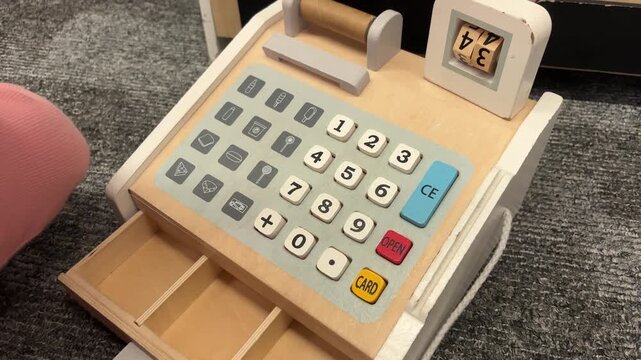 A child pulls open the drawer of a wooden toy cash register on a carpet, pretend shopping, motor skills, childhood learning.