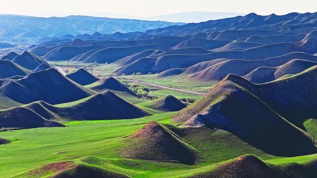Aerial view of rolling green hills and a winding road through grasslands in summer, Xinjiang, China.