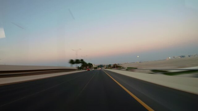 Abu Dhabi, UAE, timelapse driving along a wide highway from dusk into night, car taillights and street lights stretching into light trails with the motion