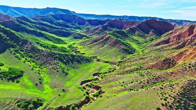 Aerial view of rolling green hills and an eroded canyon landscape along the S101 highway in Xinjiang, China.