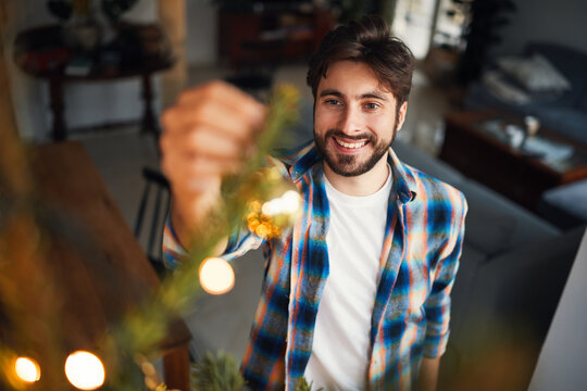 Smiling young man decorating christmas tree at home