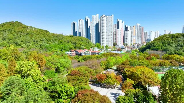  4K aerial drone slow-motion view of modern apartment buildings next to a colorful autumn park in South Korea.
