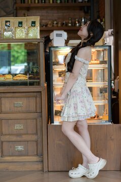 Young woman in floral dress standing beside display refrigerator in cozy cafe setting