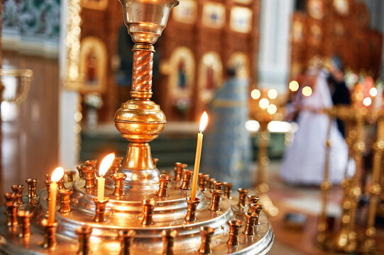 Soft-lit candles burn on brass candelabrum inside church during a wedding ceremony, creating warm, sacred atmosphere of prayer, tradition and celebration with bride and groom blurred in the background