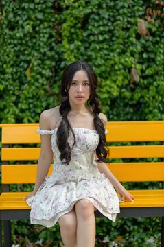 Young woman sitting on yellow park bench in a lush green garden environment