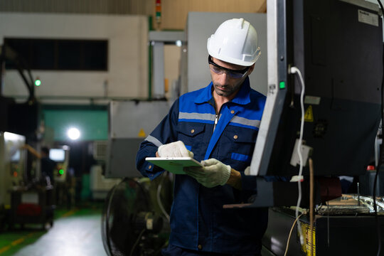 Factory technician in blue protective workwear uses a tablet to monitor industrial equipment, demonstrating digital maintenance, machine inspection and technology-driven manufacturing.