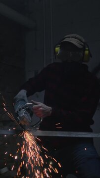 Man industrial worker or construction worker cuts metal with a grinder. Male uses a metal angle saw. Blacksmith welder is smoothing metal steel, cutting metal with bright flying sparks in a workshop