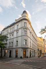 A striking historical corner building features an ornate light-colored facade and a distinctive domed turret, glowing in the soft light of golden hour in Krakow, Poland. © Danica Chang