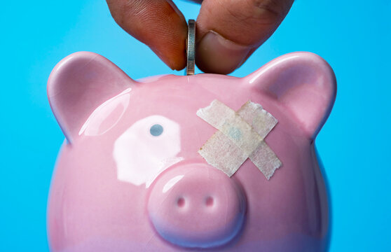 Financial recovery and saving money concept with a hand inserting a coin into piggy bank patched with tape for emergency savings, budget repair, money problems and financial resilience.