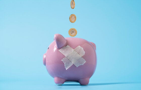 Financial recovery and emergency savings concept with coins falling into a pink piggy bank patched with tape for money problems budgeting repair, financial crisis and rebuilding savings.
