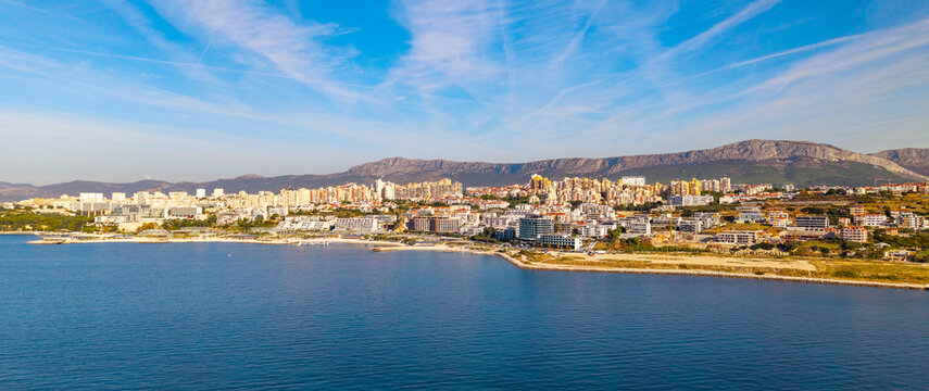 Aerial panorama of a modern coastal district in Split with contemporary apartment buildings, a waterfront promenade, landscaped park, construction sites and small beaches