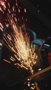 Male industrial or construction worker cuts metal with a angle grinder. Man uses circular saw at garage or workplace. Cutting raw material with flying red sparks at the factory or plant. Slow motion