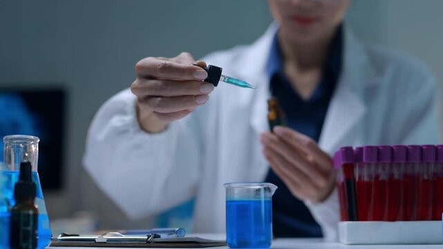 Female scientist adding drop of liquid reagent from a pipette into a beaker during a scientific experiment in a laboratory
