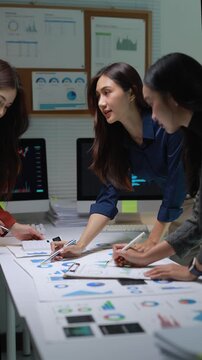 Business women collaborating and analyzing financial data charts during a corporate meeting in a modern office at night