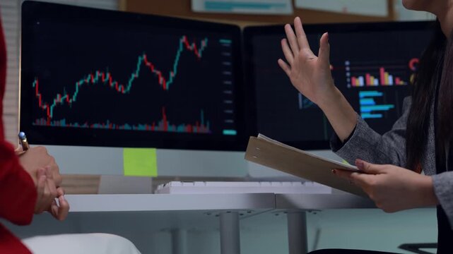Financial analysts discussing cryptocurrency stock market data on dual computer monitors in the office