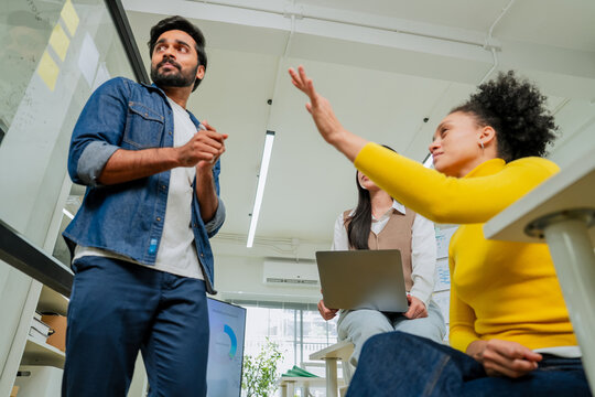 Young businesswoman raising hand to share idea during team meeting with colleagues in modern office