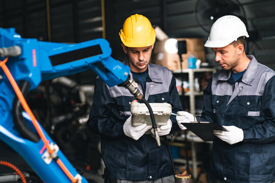 Industrial worker mechanical engineer factory inspection two male technicians examine robotic equipment while using tablet in workshop, showing focused teamwork and modern manufacturing expertise
