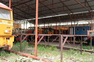 Railway locomotive yellow train industrial depot covered rail yard vintage railway locomotive parked beside weathered rail equipment and blue maintenance building large steel canopy, creating © chokniti