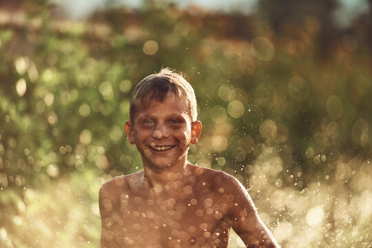 Happy Boy Splashing in Water On a Sunny Summer Day With Bokeh Background and Golden Light