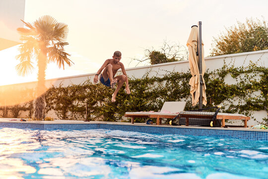 Boy Jumping Into a Backyard Swimming Pool on a Sunny Summer Afternoon