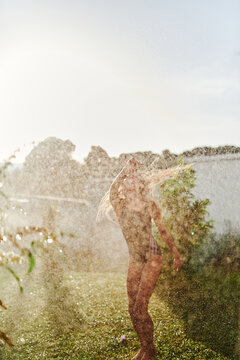 Young Woman Playing in Backyard Sprinkler on Sunny Summer Day Enjoying Water and Freedom