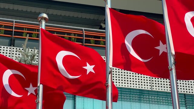 Close up view of Turkish flag with crescent and star on red background waving on a metal pole in a city park in Istanbul, modern urban architecture, national pride and civic identity concept