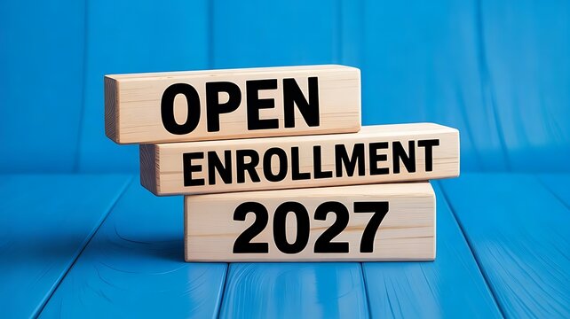Stack of wooden blocks with the text open enrollment 2027 on a blue wooden surface representing health insurance and benefits registration time frame