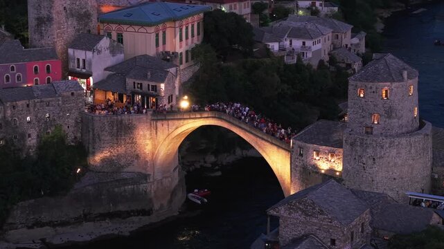 Aerial view of the historic Old Bridge (Stari Most) surrounded by traditional stone buildings, historic towers, and red-roofed houses in the old town at dusk in Mostar, Bosnia and Herzegovina