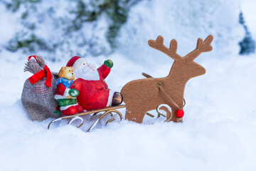 Santa Claus figurine with teddy bear and sack on sleigh pulled by wooden reindeer in snowy winter background with copy space © Jurga Jot