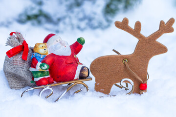 Santa Claus figurine with teddy bear and sack on sleigh pulled by wooden reindeer in snowy winter background with copy space © Jurga Jot